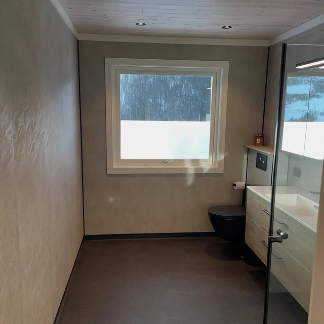 Nyrenovert bad med mørkt gulv, dusjvegger i glass og moderne servant med speil.